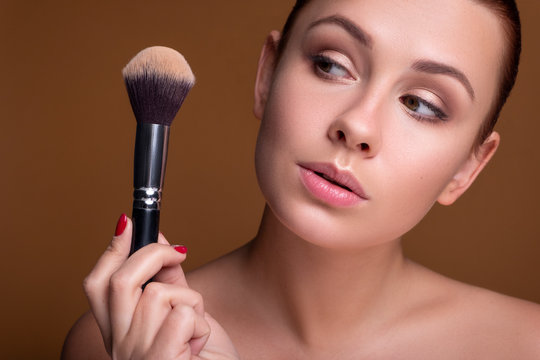 Caucasian brunette woman apply blush on a cheekbone with a brush. Close up portarait. Skin care  concept