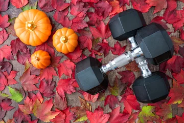 Fototapete Wasserfälle Pair of crossed dumbbells on a rustic wood background covered in fall color of red, green, yellow, and orange maple leaves, with ceramic pumpkins  © knelson20