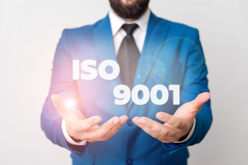 Text sign showing Iso 9001. Business photo showcasing designed help organizations to ensure meet the needs of customers Man with opened hands in fron of the table. Mobile phone and notes on the table