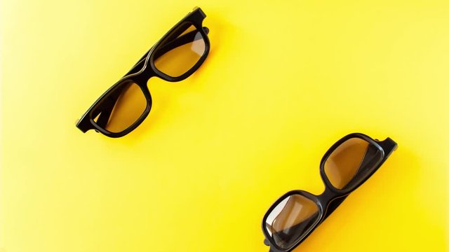 Stop motion animation of view from above of two pair 3D black glasses danсing with each other on yellow background 