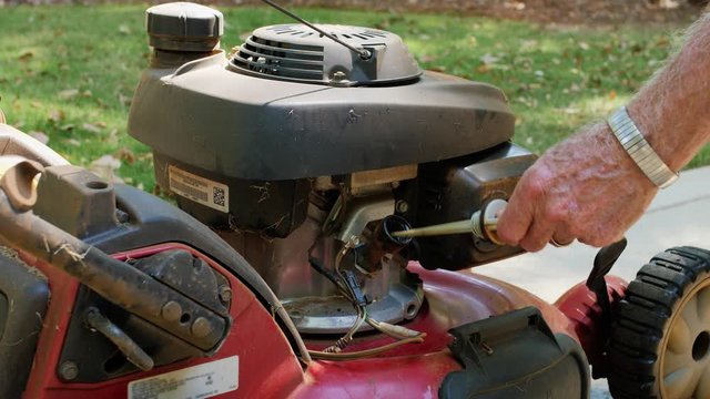 Male landscaper checking engine oil level on gas powered lawn mower. Checking dipstick for proper oil level.