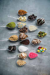 Food in spoons. Variety of  chocolate, hazelnut, peanut, pistachio, bonbon, wafer rolls, white chocolates, dark chocolates, milky chocolates, bite dessert, granulated sugar, crunch, coconut powder