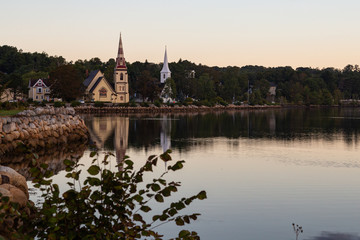 Three churches along the waterfront in Mahone Bay, Nova Scotia, reflected in the water at sunrise on a beautiful morning.