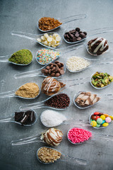 Food in spoons. Variety of  chocolate, hazelnut, peanut, pistachio, bonbon, wafer rolls, white chocolates, dark chocolates, milky chocolates, bite dessert, granulated sugar, crunch, coconut powder