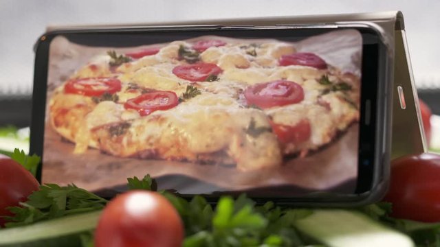 Cellphone with baked italian pizza in the oven on screen in microwave. Plate with salad and mobile phone with cooking food footage on screen rotating in microwave.