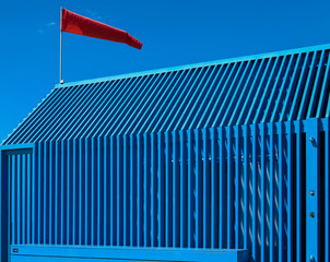 Blue ripped wooden house with red wind strength and direction on top. - obrazy, fototapety, plakaty
