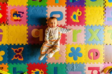 Baby doing exercise by shaking his legs in his toy room, on colorful quilted floor.