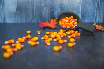 scoop ladle of autumn fall halloween candy corn spilled on black slate with fall autumn leaves