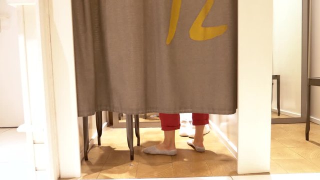 female legs are visible from under the curtains in the fitting room of a clothing store.