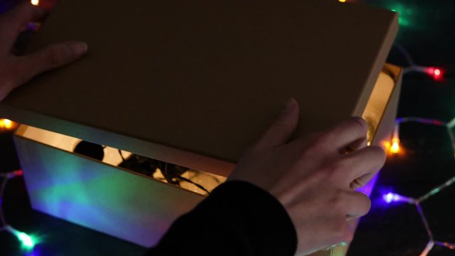 woman opening mystery box in the dark and revealing bright light coming from the inside due to string lightbulbs in it,