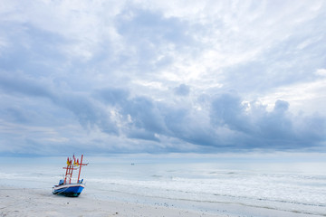 view of blue fisheries boat on a beach with cloudy sky and sea 