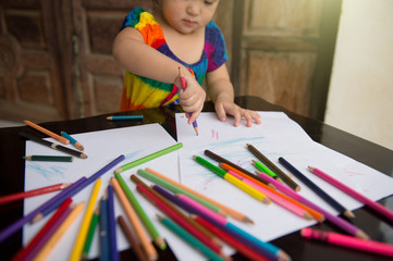 little girl learn to draw and paint with various pencil colour and white paper on wooden desk, family relationship concept, home school, holding pencil colour