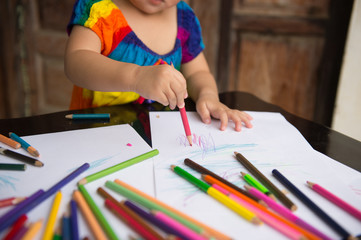 little girl learn to draw and paint with various pencil colour and white paper on wooden desk,...