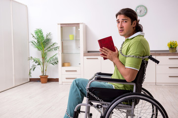 Young male invalid in wheel-chair suffering at home