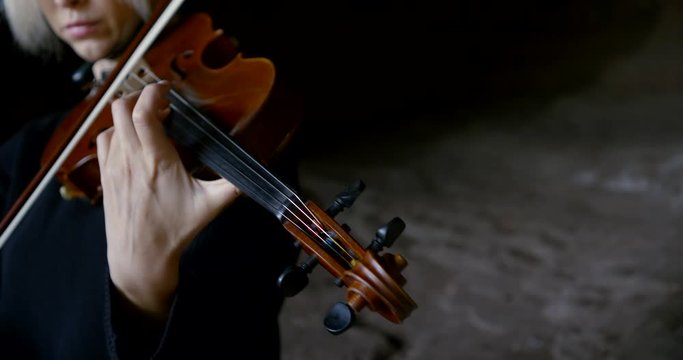professional musician plays brown wooden violin in darkness
