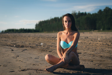 Fototapeta na wymiar Young woman in a turquoise swimsuit near the water sunbathing on the beach