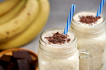 Banana milkshake in a glass with chocolate on grey concrete surface, closeup