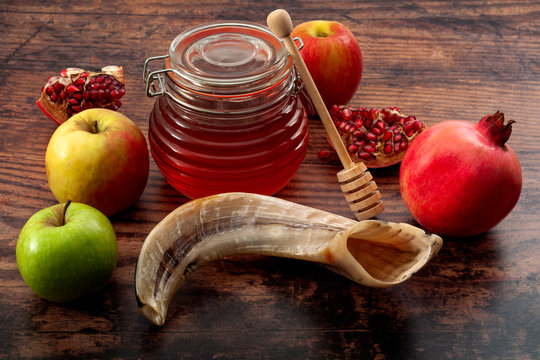 Happy Rosh Hashanah, judaism, traditional autumn holiday in jewish culture and judaic new year conceptual idea with ram horn or shofar, jar of honey, apple and pomegranate isolated on wood background