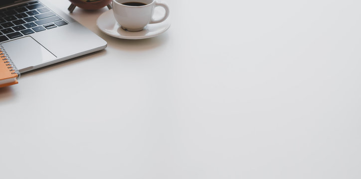 Minimal workplace with laptop computer, coffee cup and office supplies on white wooden desk