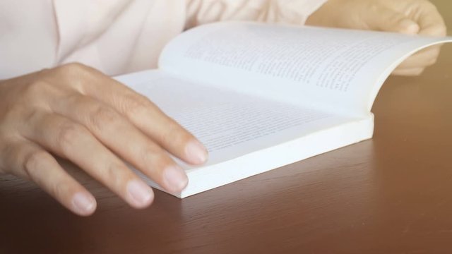 4K. woman reading textbook , using hand flip on each page from paper corner on wooden table with sunlight shining from the window