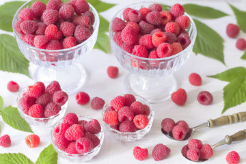 ripe raspberries in cups and spoons on a white background. raspberry with leaves closeup. background with fresh organic raspberries on the table.