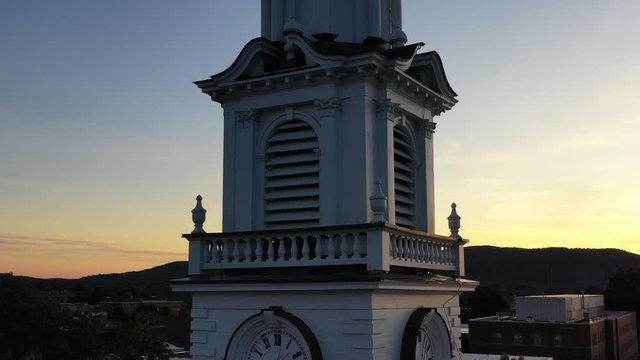 Wooden white church steeple with clock at sunset in New England, 4K close drone shot rising up