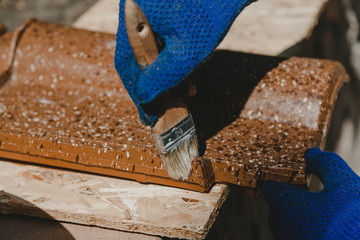 Gloved hands paint shingles with brush