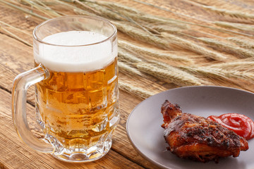 Glass of beer, plate with grilled chicken and ears of barley on a wooden background.