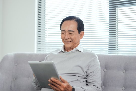 Happy Senior Relaxing At Home And Using Tablet.