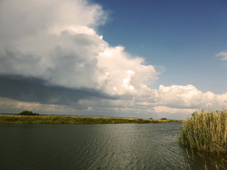 Beautiful big clouds in blue sky over river and steppe, autumn, reeds