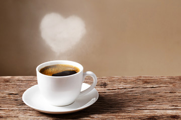 Heart of steam hovering over a red coffee cup of coffee on wooden table with cream wall background.