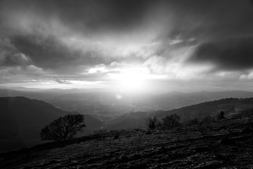Moody sunset on Monte Cucco (Umbria, Italy), with tree in the foreground and sun filtering through clouds
