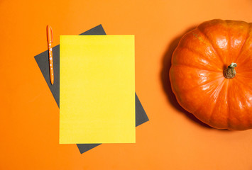 Halloween holiday concept.  Two sheets of paper, a pen, a large pumpkin on an orange background. Free space for your text.