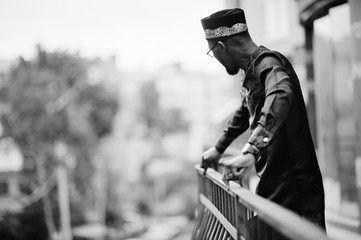Handsome afro american man wearing traditional clothes, cap and eyeglasses in modern city on...