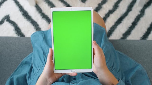 Woman uses tablet with green screen for watching video, shopping online and texting in social networks. 4k slow motion footage.  Top view.