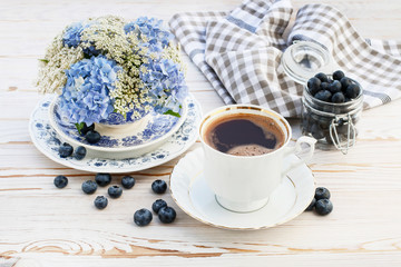 Cup of coffee and floral arrangement with blue hortensia