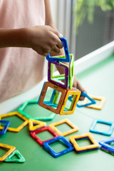 Girl in pink dress playing with magnetic geometric shape toy, hands show, no face.
