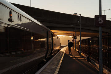 station silhouette of a tourist with a backpack who is going to take a train at sunset