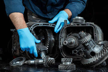 Hands of a male repairman in blue gloves on a background of a gearbox, close-up. Repair box...