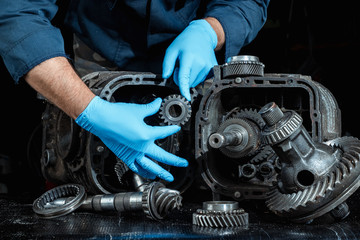 Hands of a male repairman in blue gloves on a background of a gearbox, close-up. Repair box predach, repair of used cars. Metal background