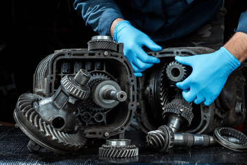 Hands of a male repairman in blue gloves on a background of a gearbox, close-up. Repair box predach, repair of used cars. Metal background