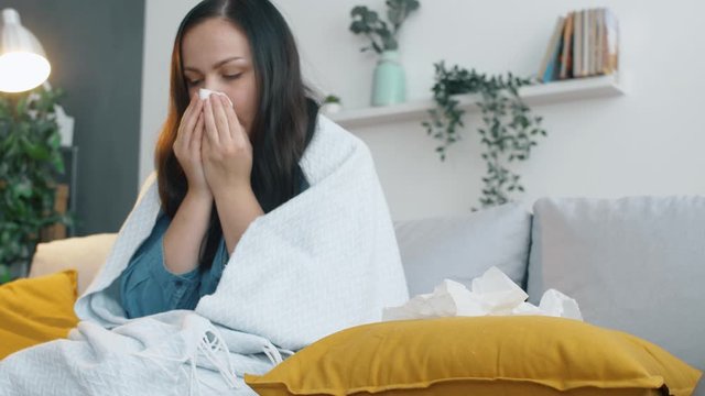 Sick woman with plaid sits on sofa and coughs. The girl has a cold and is treated at home on the sofa. 4k footage.