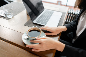 Young woman drinking fragrant coffee. Female holding cup. Girl Sitting in coffee shop at wooden table. large Windows, panorama of the city