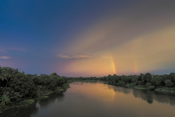 River view sunset of Mae Klong River around with green forest on both bank with yellow sun light and rainbow in cloudy sky background, Ban Pong, Ratchaburi, Thailand.