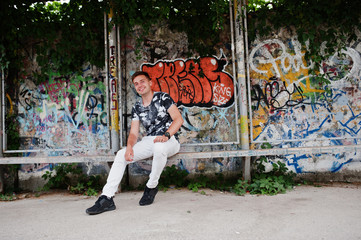 Lifestyle portrait of handsome man posing on the street of city with graffiti wall.