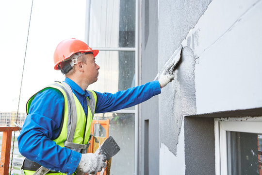 Facade worker plastering external wall of building