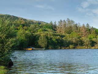Small fishing boats on a lake Corrib, Ireland, Hill covered with trees, Blue cloudy sky.