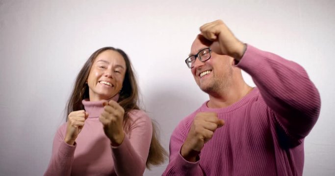 cheerful man and woman are rejoicing and dancing in room, showing thumbs up, kissing