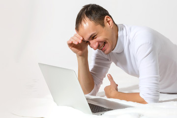 Surfing web at home. Cheerful young man lying on the floor with laptop, isolated over white background