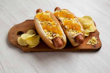 Homemade colombian hot dogs with pineapple sauce, chips and mayo ketchup on a rustic wooden board on a white wooden background, side view. Close-up.